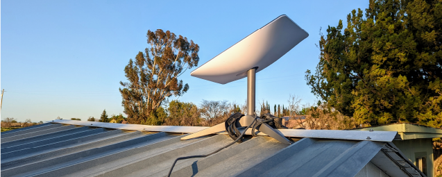 Fotografía de antena starlink sobre el techo de una casa con árboles de fondo